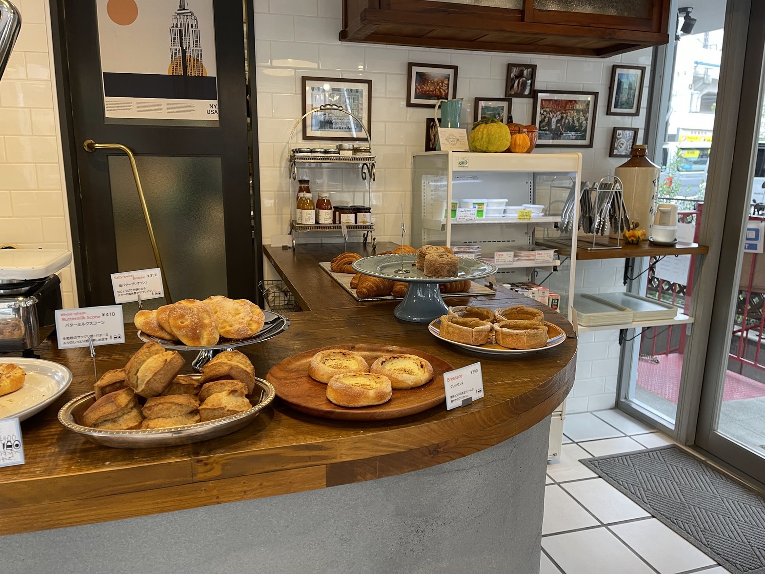NYのポスターや額縁写真が壁に並ぶ店内カウンターに、バタースコーン・ブレッサンド・クロワッサンなど複数のパンが皿に盛られて並ぶ